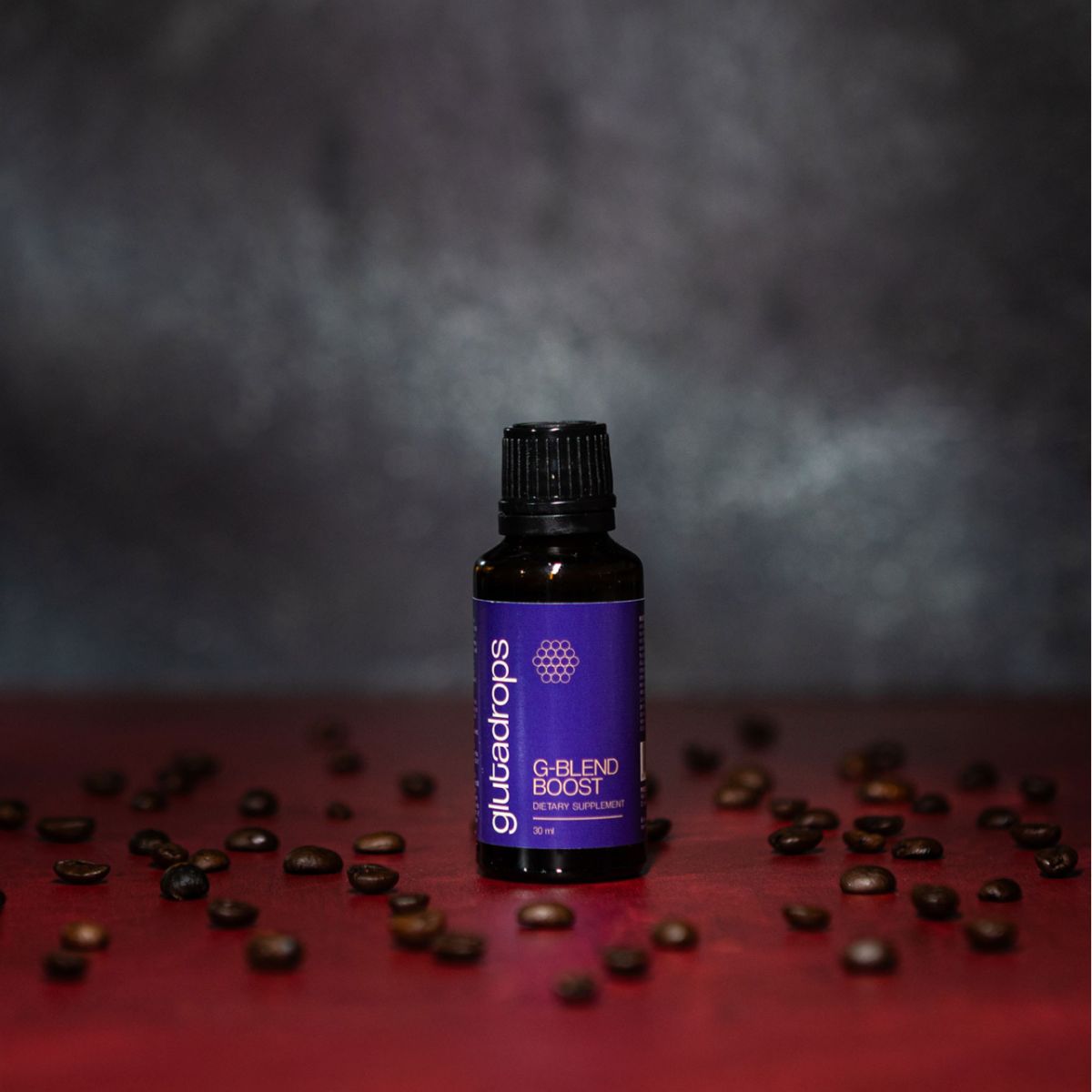 Braune Glasflasche mit schwarzem Deckel und blauer Etikette. Aufschrift: Glutadrops, G-Blend Boost, 30 ml. Auf rotem Tisch, Kaffeebohnen.