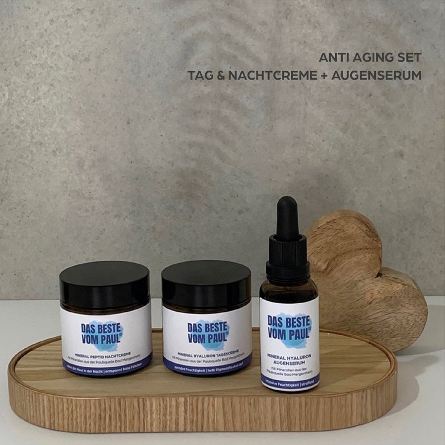 Drei Produkte auf einem Holztablett: Tagescreme, Nachtcreme und Augenserum. Text: ANTI AGING SET.