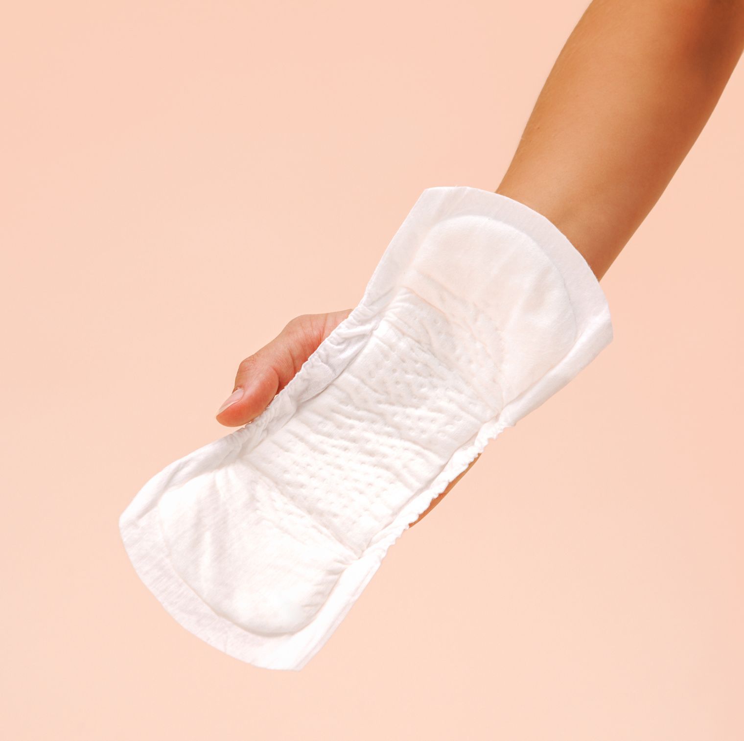 Weißes Inkontinenzprodukt, gehalten von einer Hand. Oberseite mit geriffelter Struktur. Auf rosa Hintergrund.