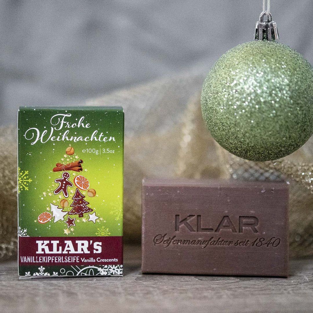 Braune Seife mit Prägung "KLAR". Grüne Verpackung mit Weihnachtsbaum-Motiv und Schriftzug "Frohe Weihnachten".