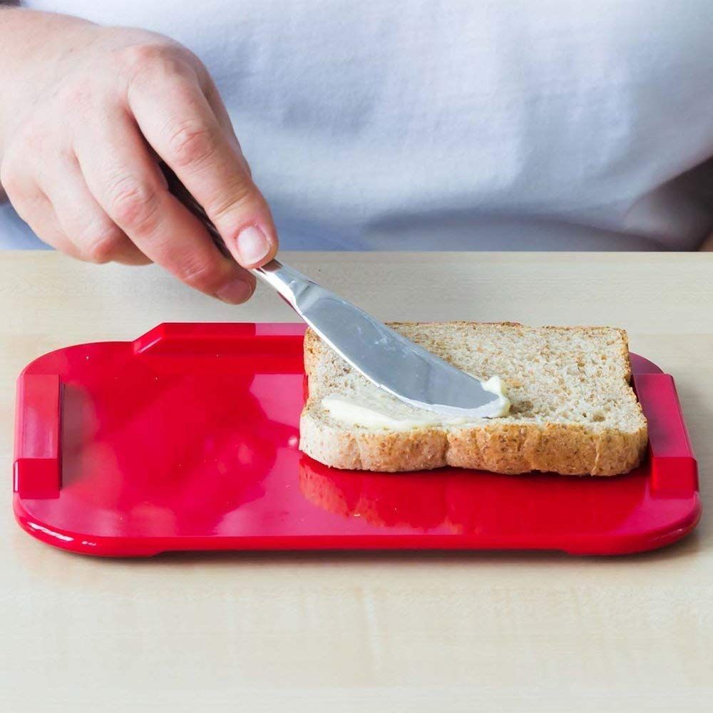 Rotes Essbrettchen mit Toastbrot und Butter. Person schmiert Butter auf das Brot mit einem Messer.