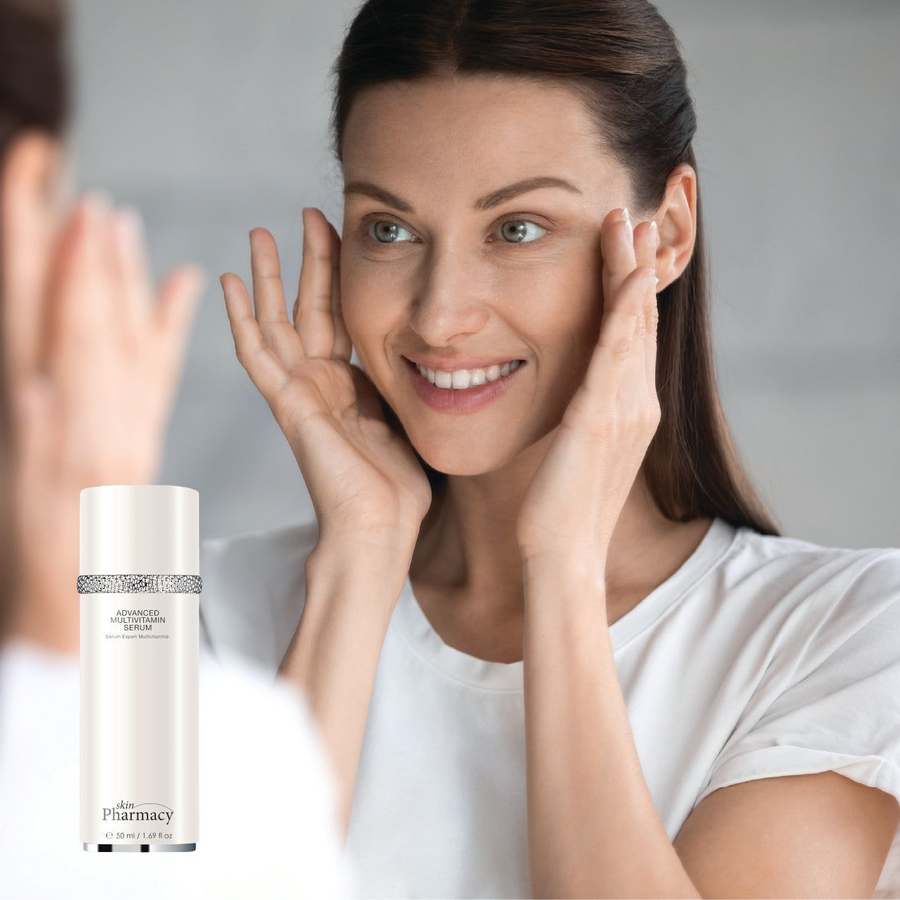 Frau betrachtet sich im Spiegel. In der Hand: weißes Serum mit silbernem Ring. Aufschrift: Advanced Multi-Vitamin Serum. Marke: skinPharmacy.
