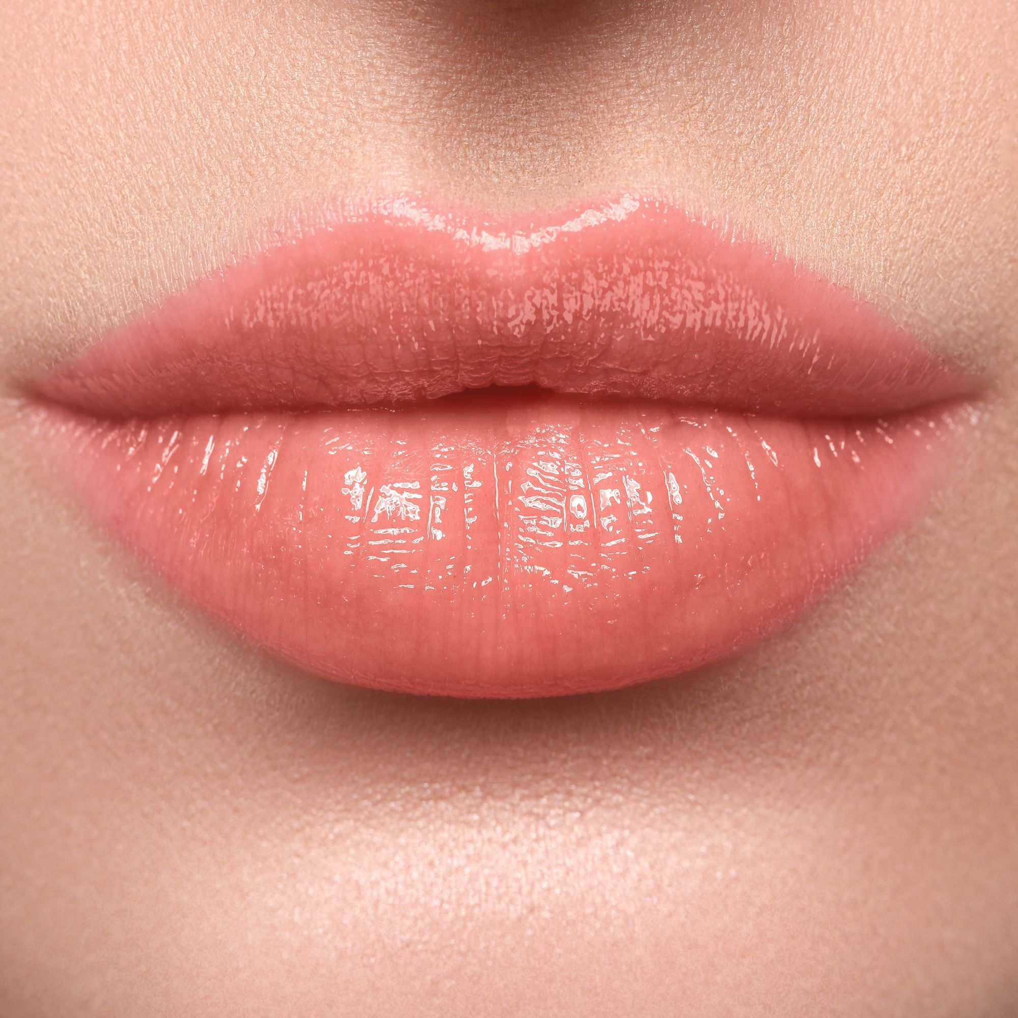 Nahaufnahme von Lippen, die mit einem glänzenden Korall-farbenen Lippenstift bemalt sind.