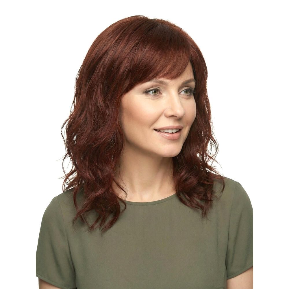 Frau mit rotbrauner Perücke, schulterlang, mit Pony. Sie trägt ein grünes Oberteil und lächelt.