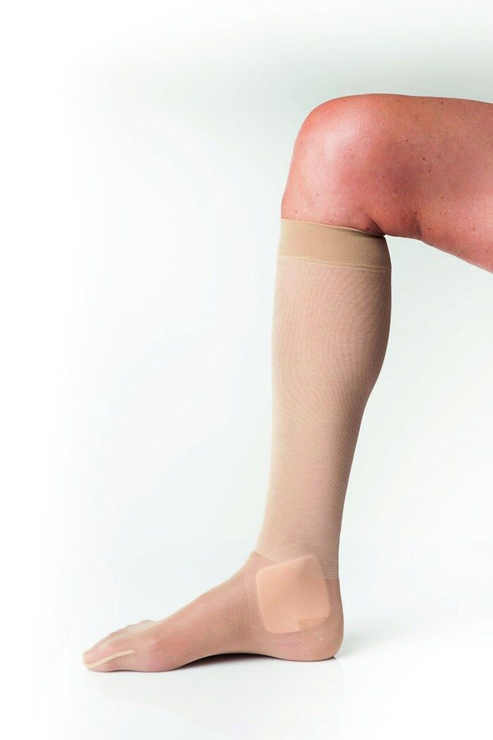 Bein mit Kompressionsstrumpf. Hautfarbener Strumpf bis zum Knie. Pflaster am Knöchel. Bein auf hellem Hintergrund.