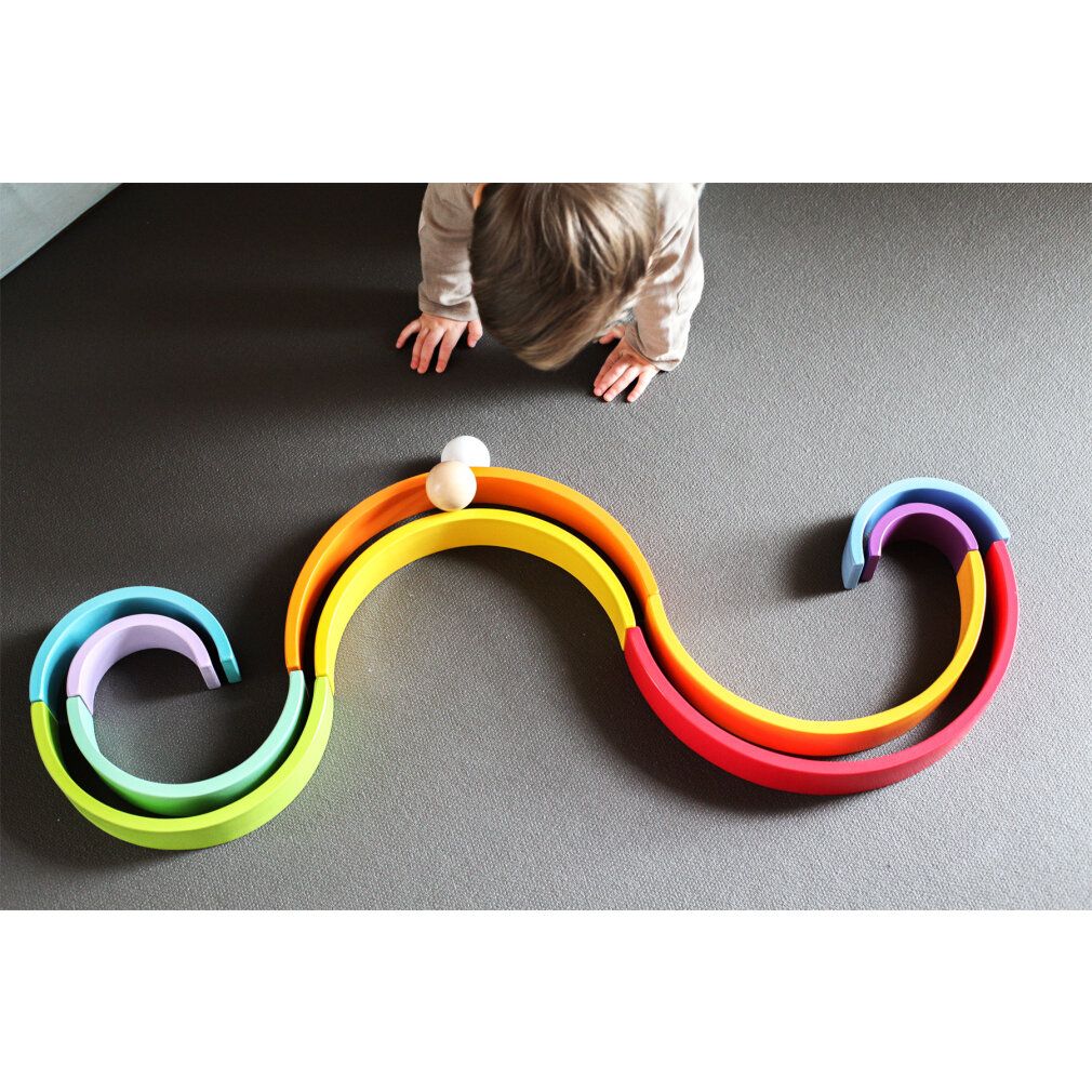 Kind spielt mit Regenbogen-Holzbausteinen. Holzbausteine in Regenbogenfarben, verschiedene Größen. Kugel.