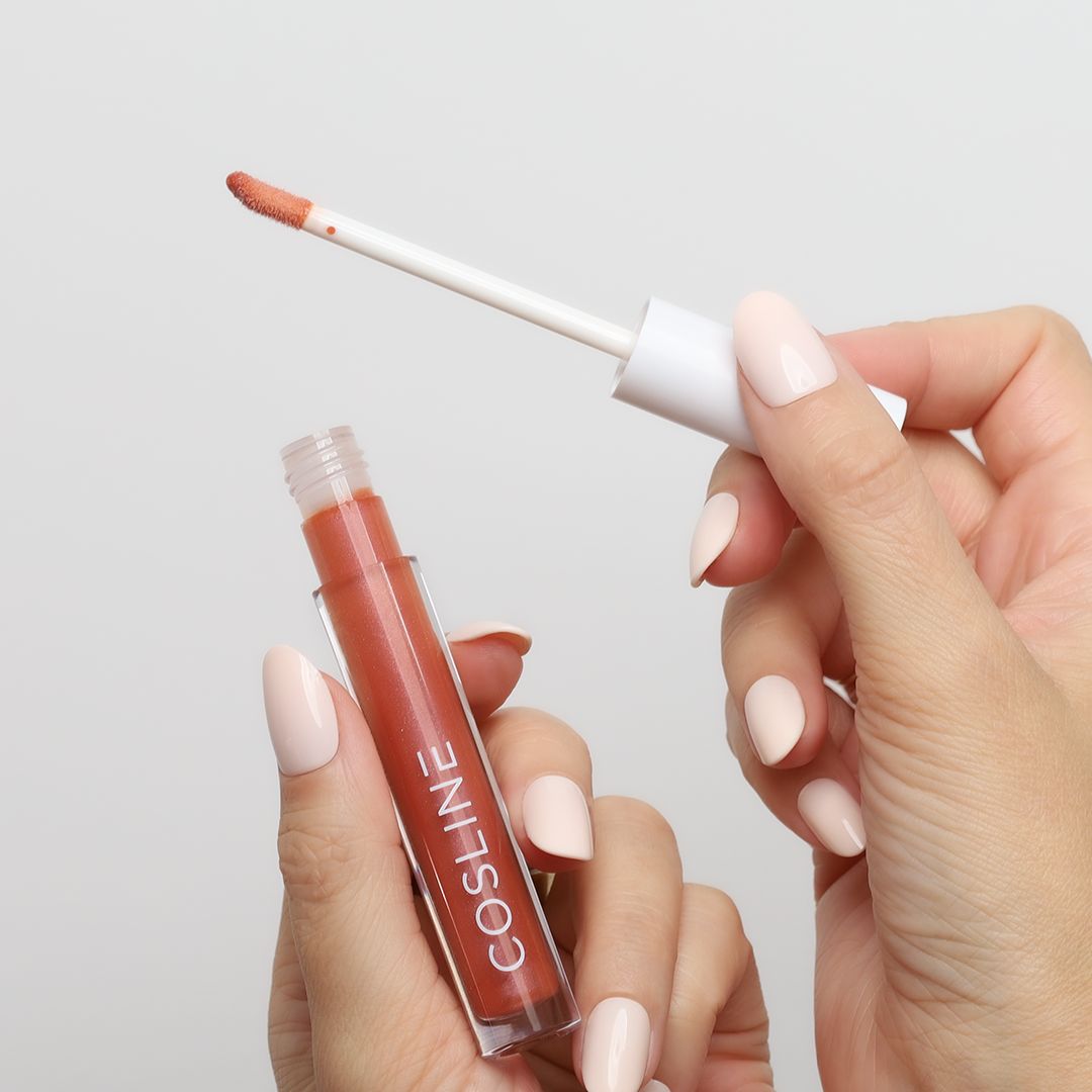 Hände halten eine geöffnete Lipgloss-Tube mit Applikator. Auf der Tube steht 'COSline'.