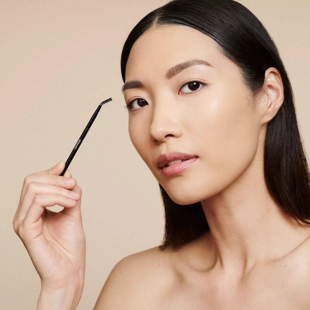 Asiatische Frau mit Augenbrauen-Styling-Pinsel. Der Pinsel wird in der Nähe der Augenbraue gehalten.