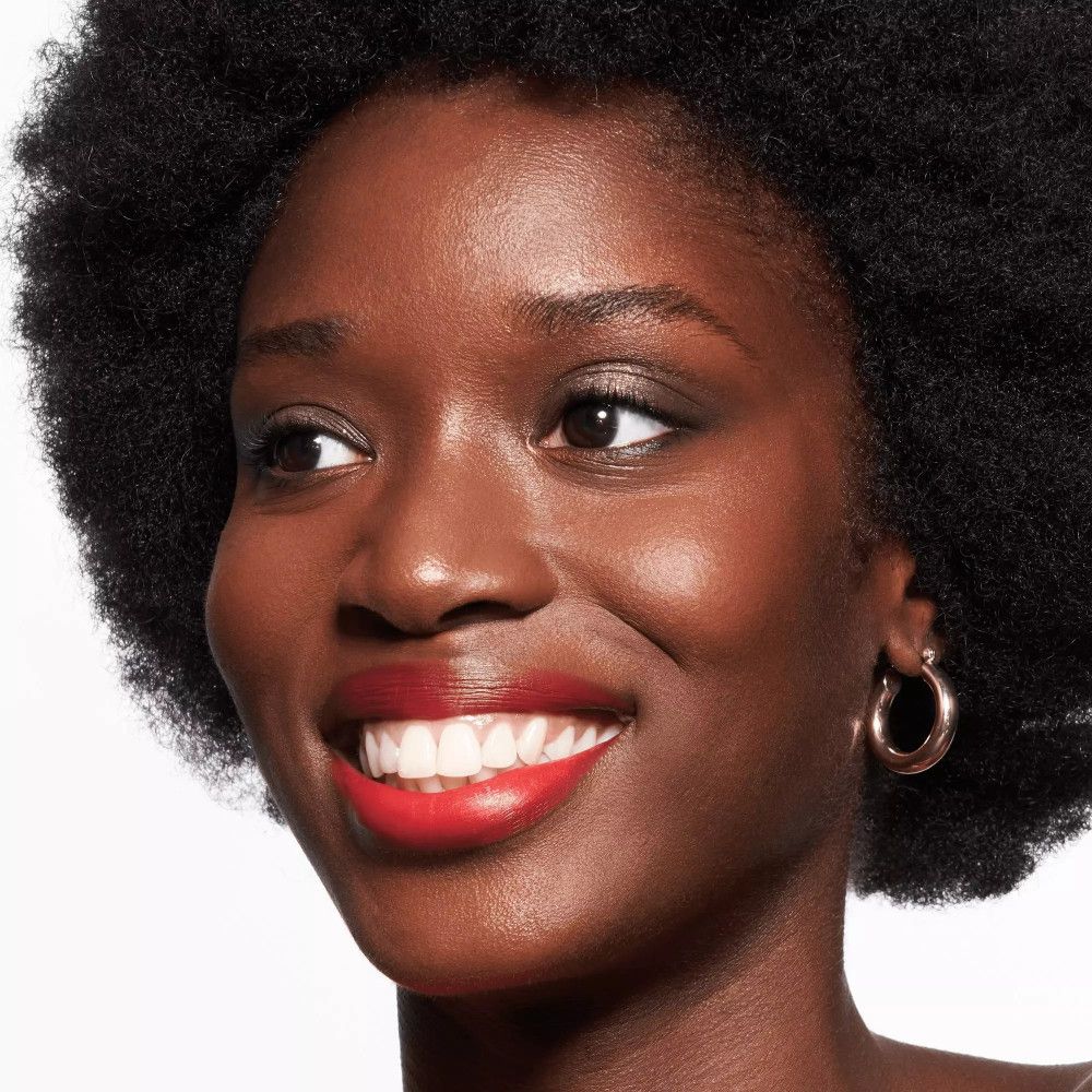 Porträt einer Frau mit rotem Lippenstift und goldenen Ohrringen. Sie lächelt.