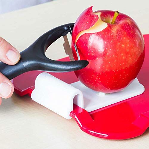 Rotes Essbrettchen mit Apfel und Schäler. Apfel wird geschält. Weiße Halterung mit Stiften.