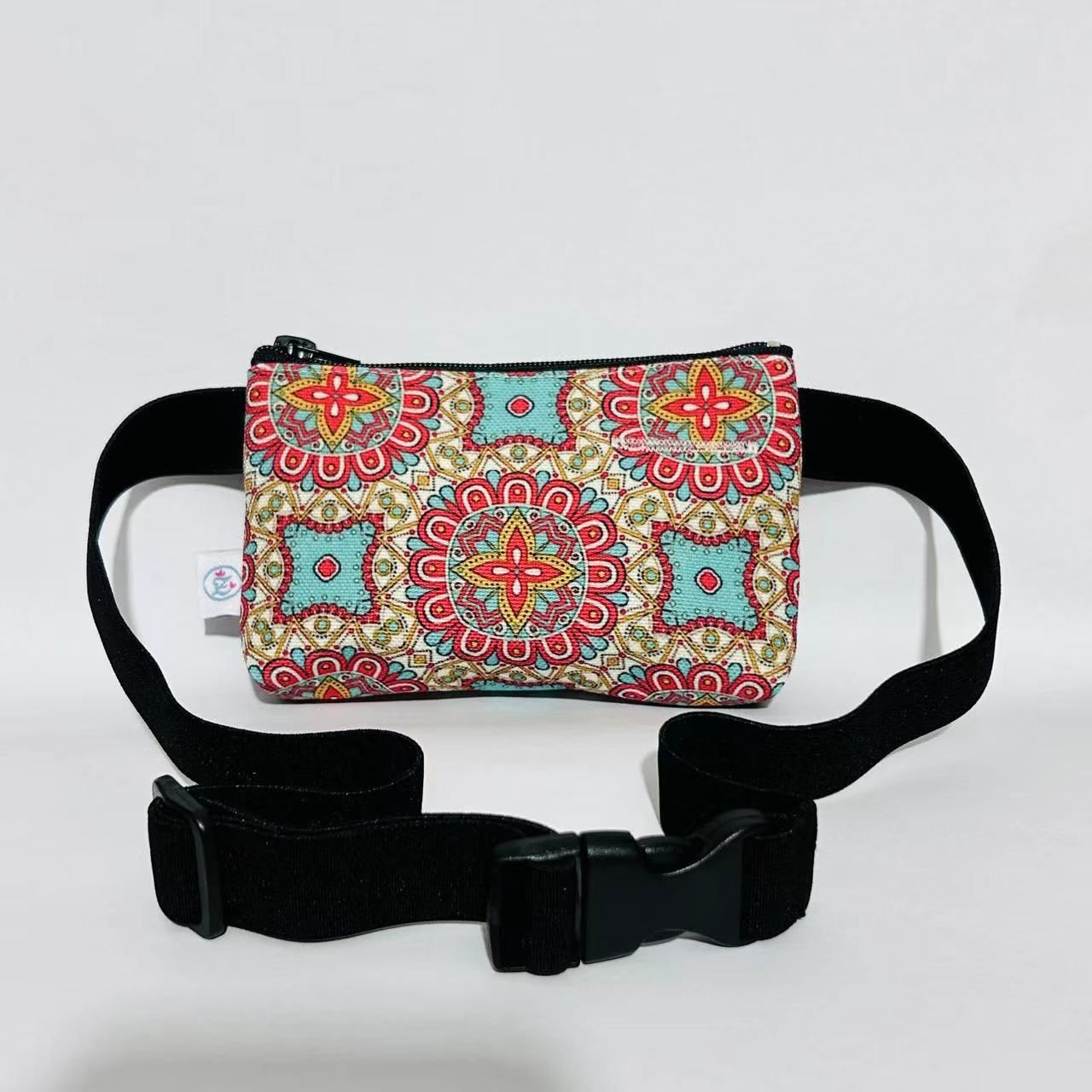 Tasche mit Mandala-Muster, schwarzes Bauchband mit Schnalle. Farbmuster: Rot, Türkis, Gelb. Kleines Etikett.