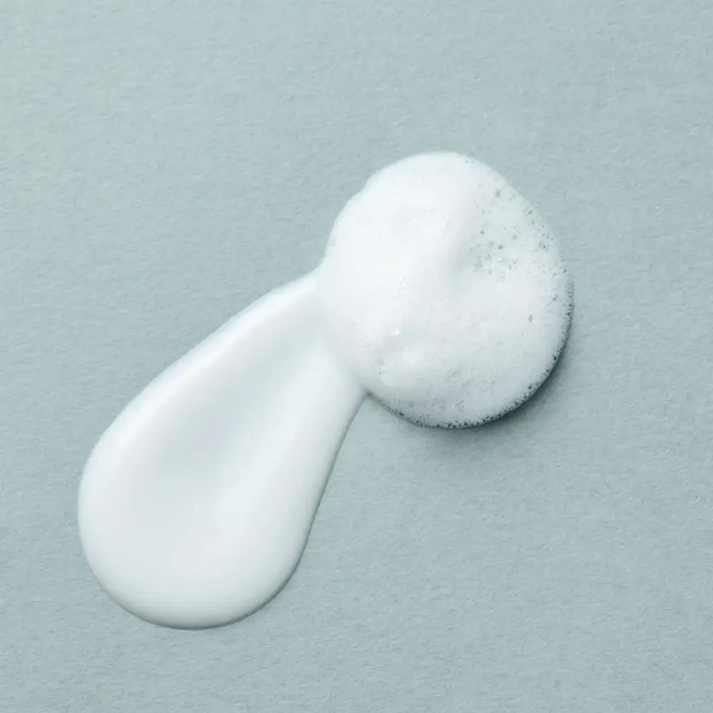 Weißer Schaum auf grauem Untergrund. Schaum und Creme. Textur. Ovale Form.