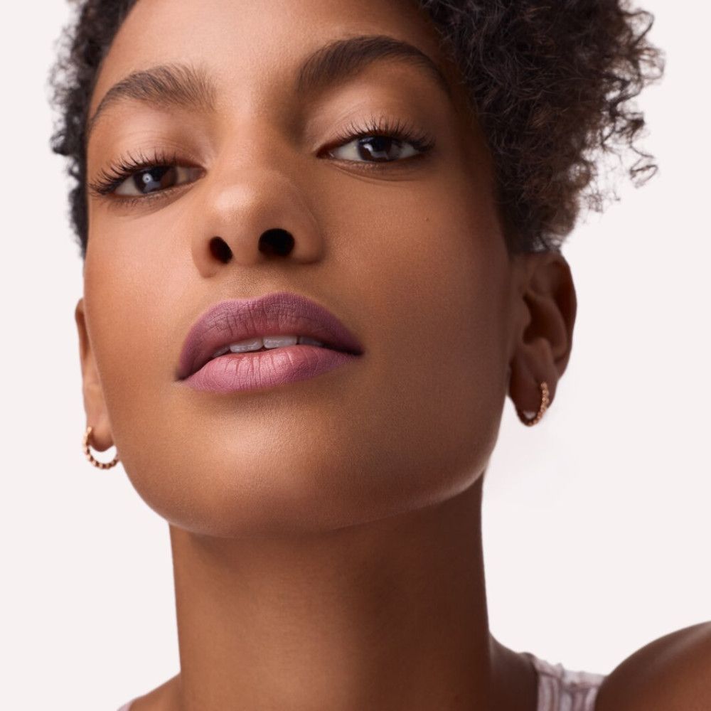 Porträt einer Frau mit Lippenstift. Rosa-braune Lippen. Goldene Ohrringe. Blick in die Kamera.