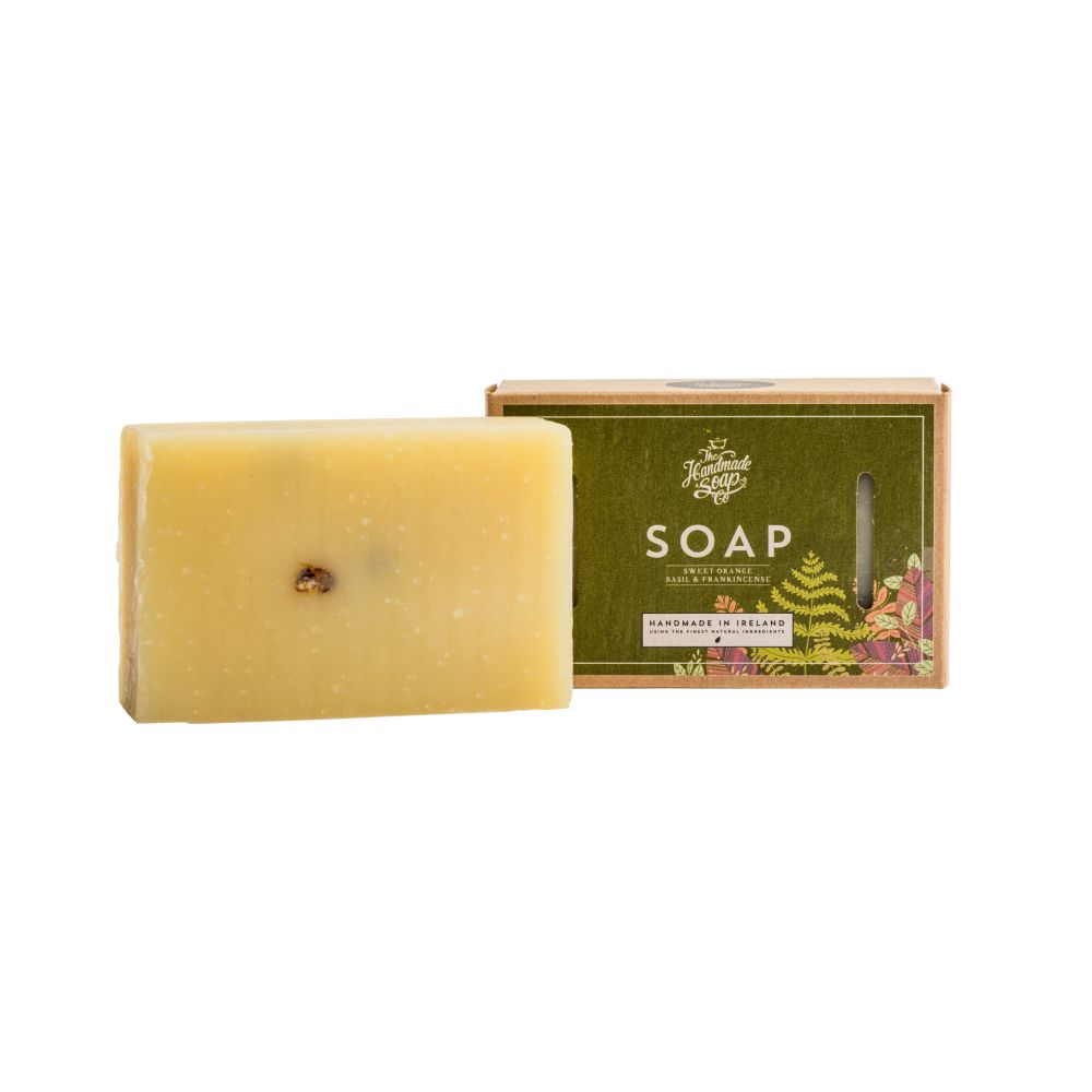 Rechteckige Seife neben Kartonverpackung. Seife hellgelb, mit dunklem Punkt. Verpackung grün mit Schriftzug SOAP und Logo.