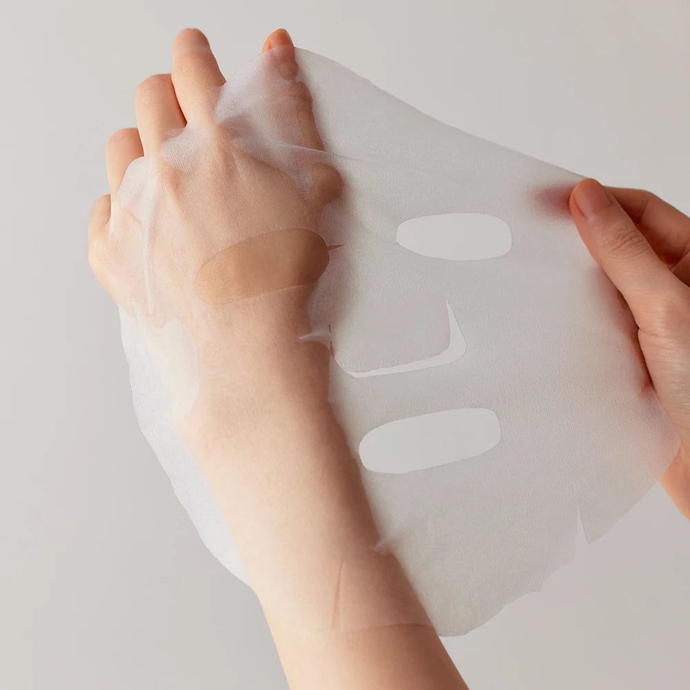 Hände halten eine Gesichtsmaske. Die Maske ist transparent mit Aussparungen für Augen und Mund.