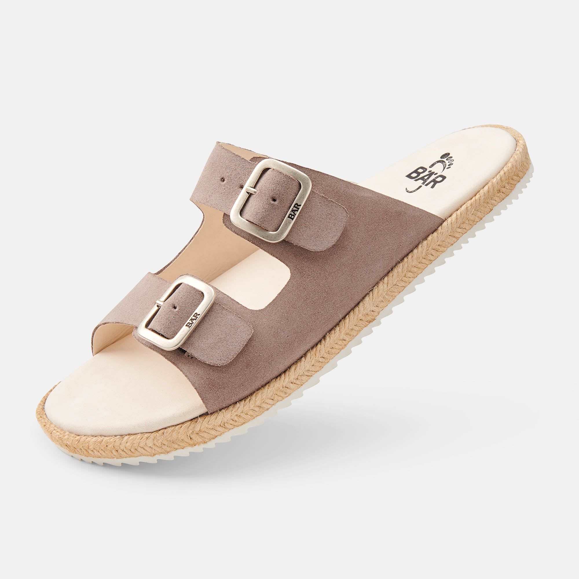 Beige Pantolette mit zwei Schnallen. Die Sohle ist weiß, der Rand geflochten. BAR ist auf den Riemen geprägt.