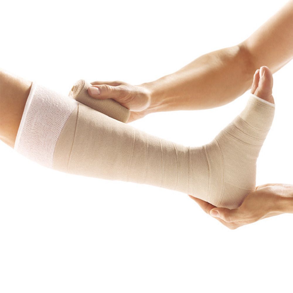 Bein mit Bandage. Eine Hand hält den Fuß, die andere wickelt die Bandage. Beige Bandage, weißer Strumpf.