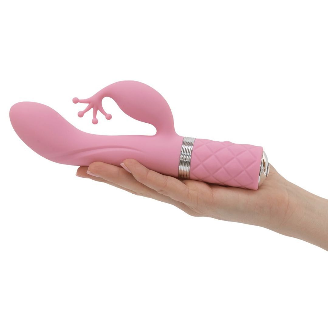 Rosa Vibrator in einer Hand gehalten. Der Griff hat ein Diamantmuster. Silberfarbene Akzente. Klitorisreizer sichtbar.