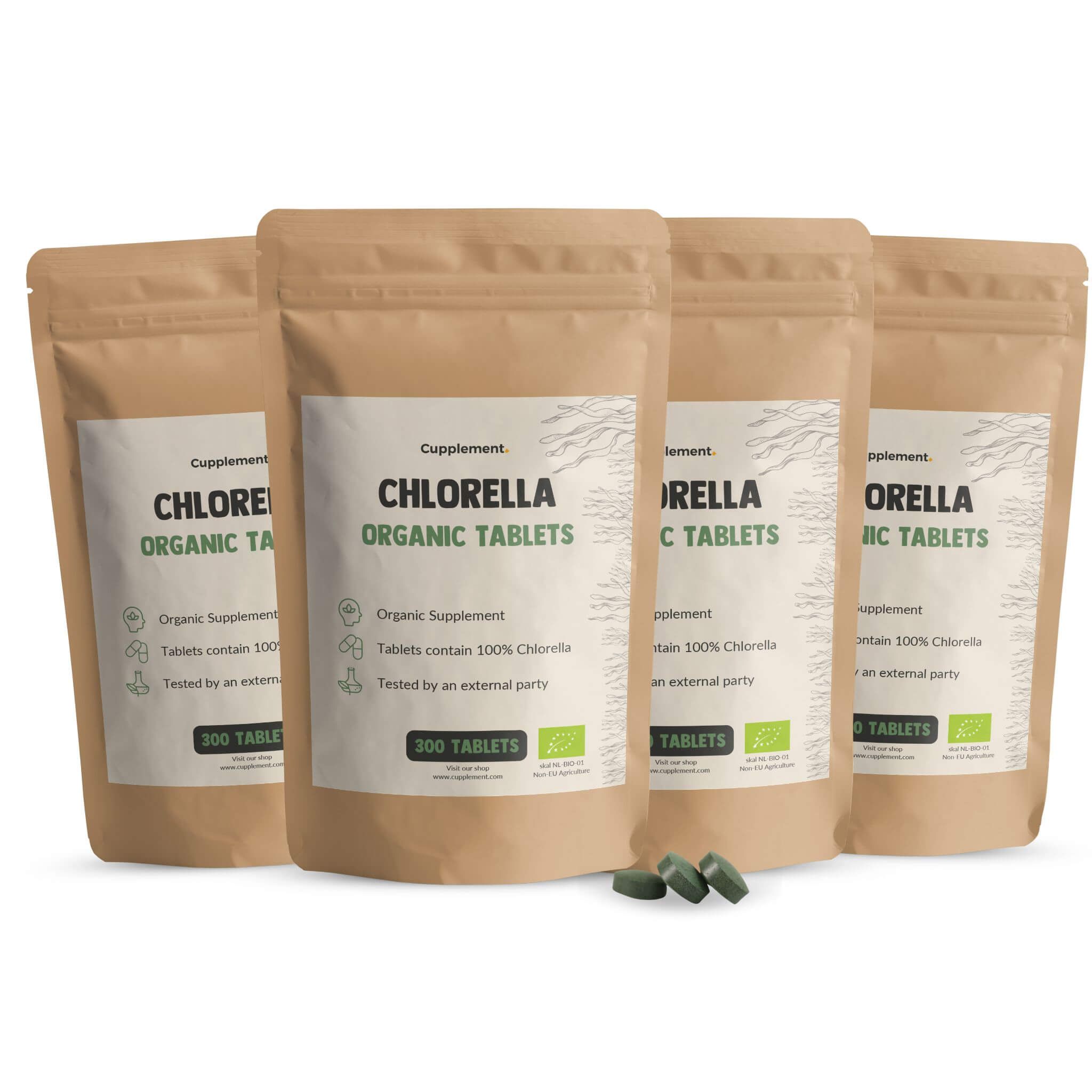 4 Beutel Cupplement Chlorella Tabletten. Braune Verpackung mit weißem Etikett. 300 Tabletten. Grüne Tabletten liegen daneben.