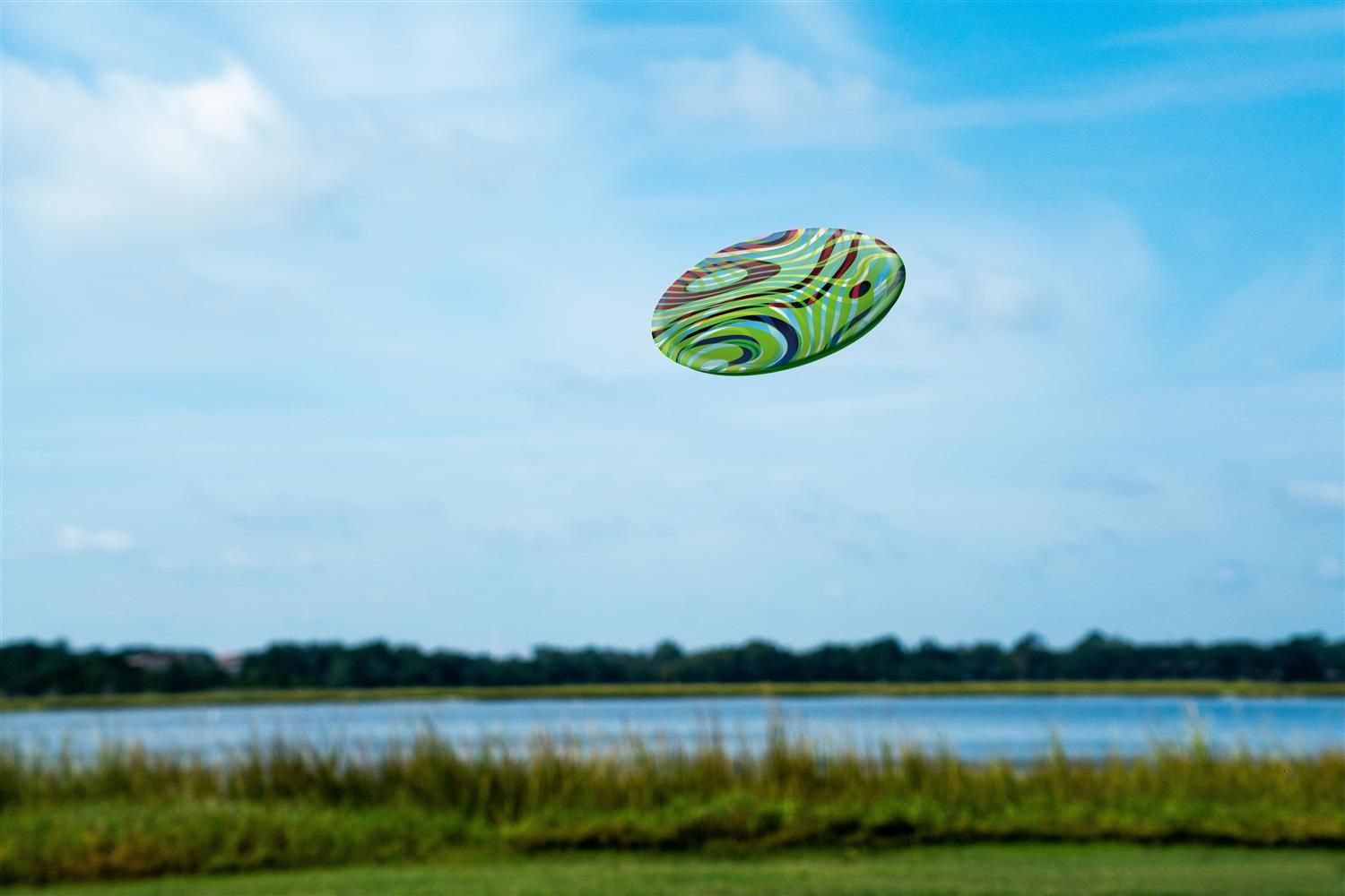 Ovale Scheibe im Flug. Farbiges Wellenmuster. Himmel und Landschaft im Hintergrund.
