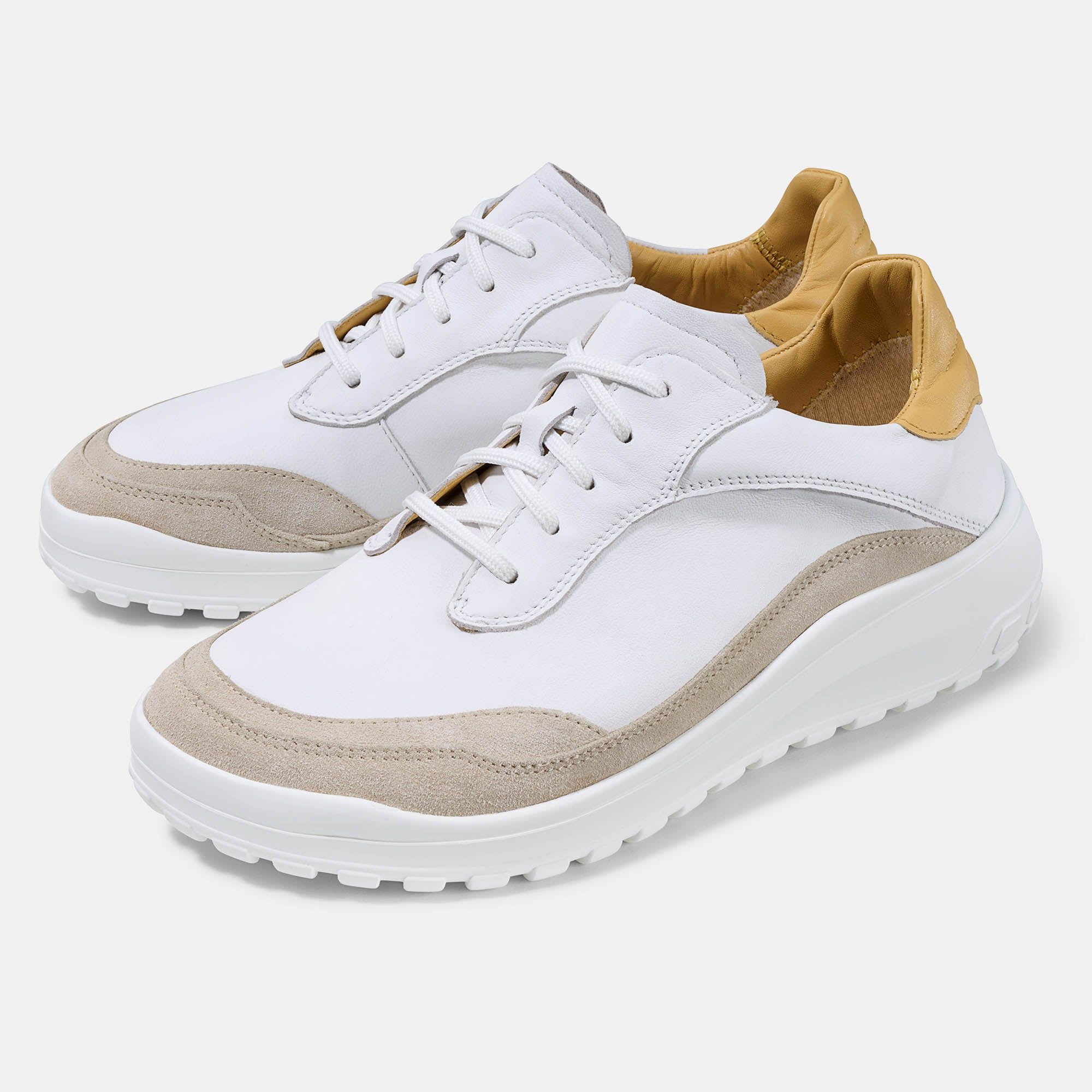 Zwei weiße Schnürschuhe mit beigen Akzenten und gelben Details. Breite Form, helles Design.