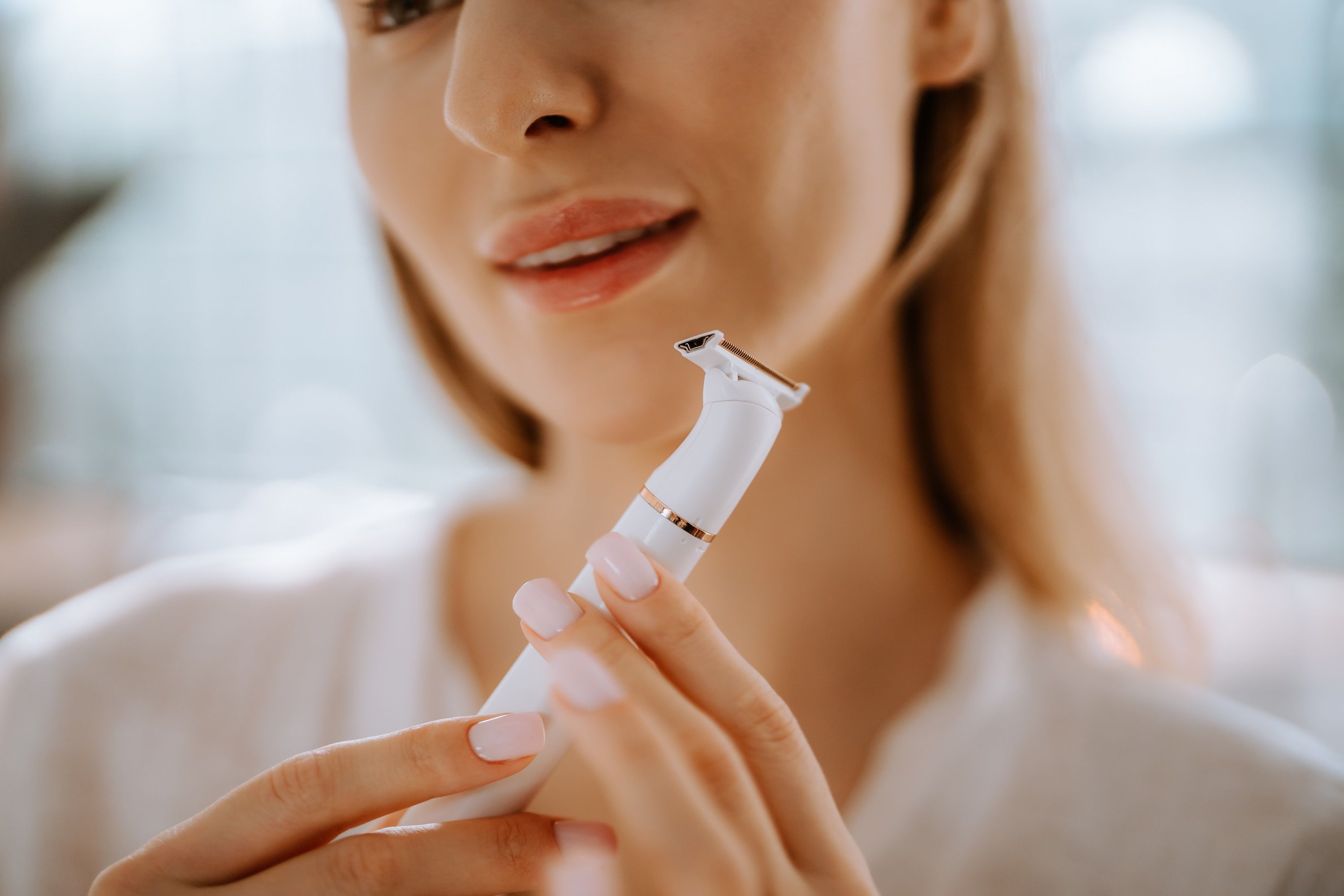 Nahaufnahme einer Person, die einen weißen Epilierer hält. Der Rasierkopf ist sichtbar.