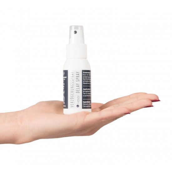 Weiße Sprühflasche in einer Hand gehalten. Schwarzes Etikett mit Aufschrift: Verzögerungsspray, Delay Spray.