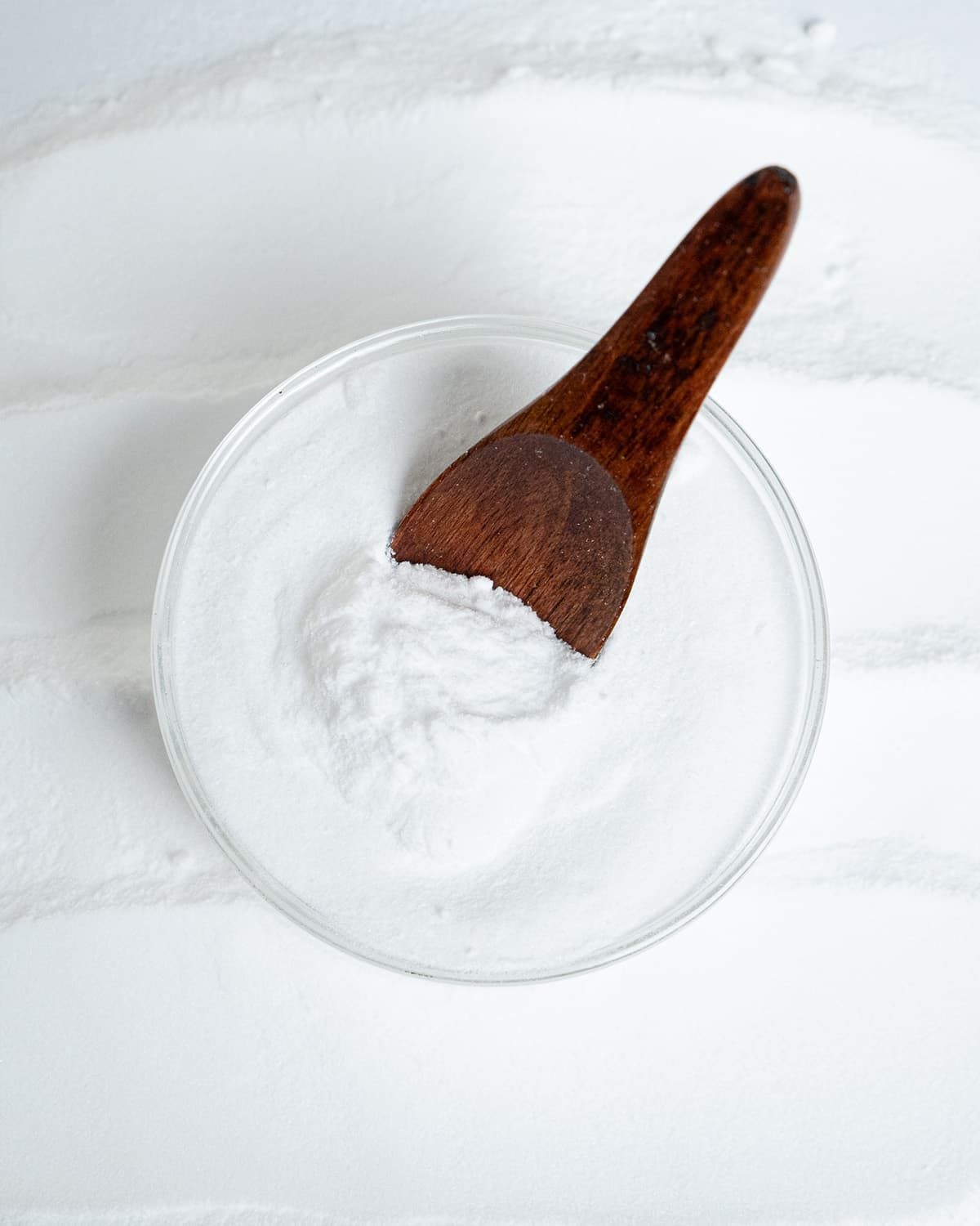 Inositol Pulver in einer Glasschale, mit einem Holzlöffel darin, umgeben von Pulver.