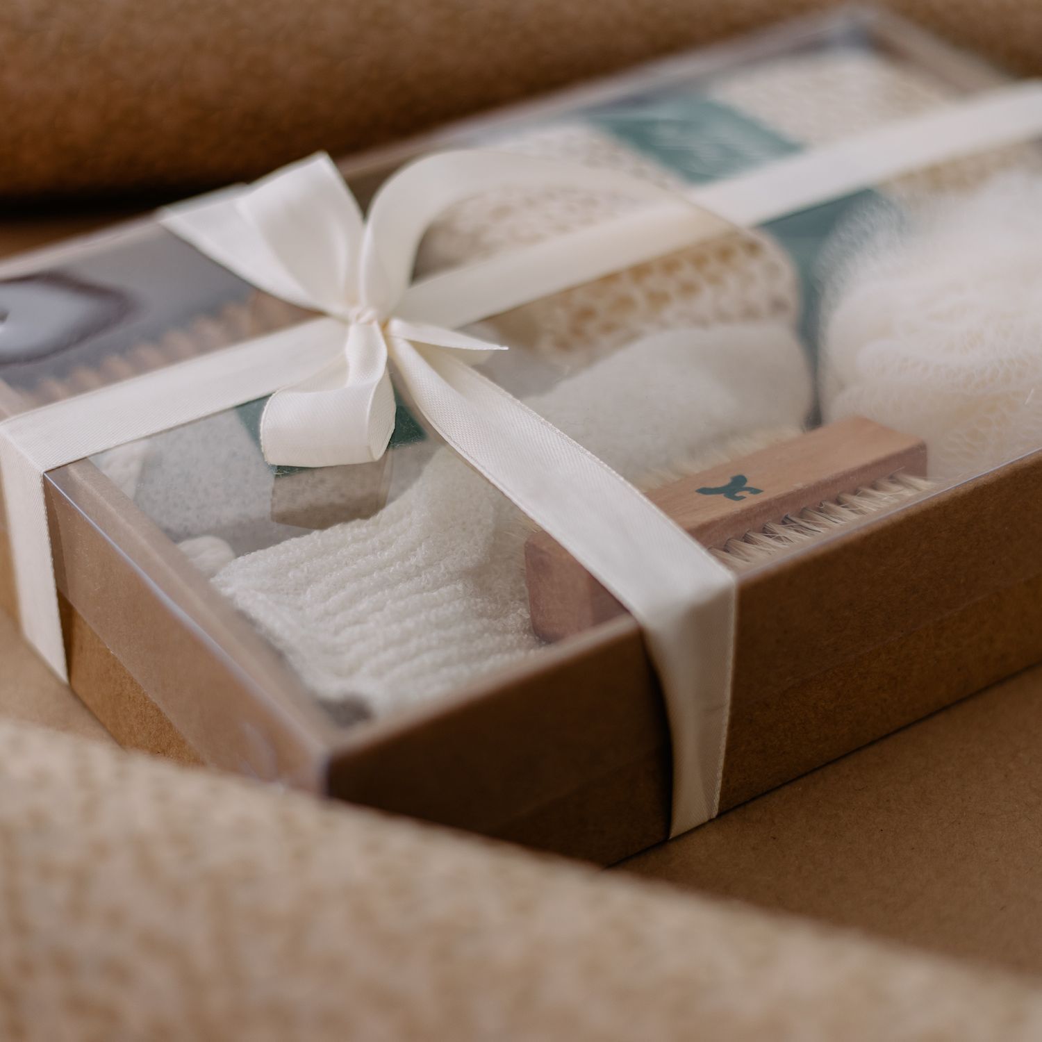 Geschenkset SPA: Nahaufnahme einer transparenten Box mit Pflegeprodukten, umwickelt mit einer weißen Schleife.