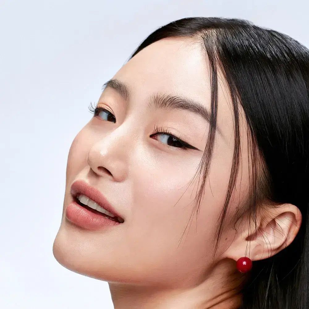 Porträt einer Frau mit dunklen Haaren und roter Ohrringe. Sie schaut zur Seite und lächelt leicht.