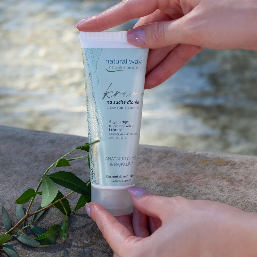 Creme-Tube, gehalten von Händen. Aufschrift: Natural Way, Creme für trockene Hände. Hintergrund: Wasser.