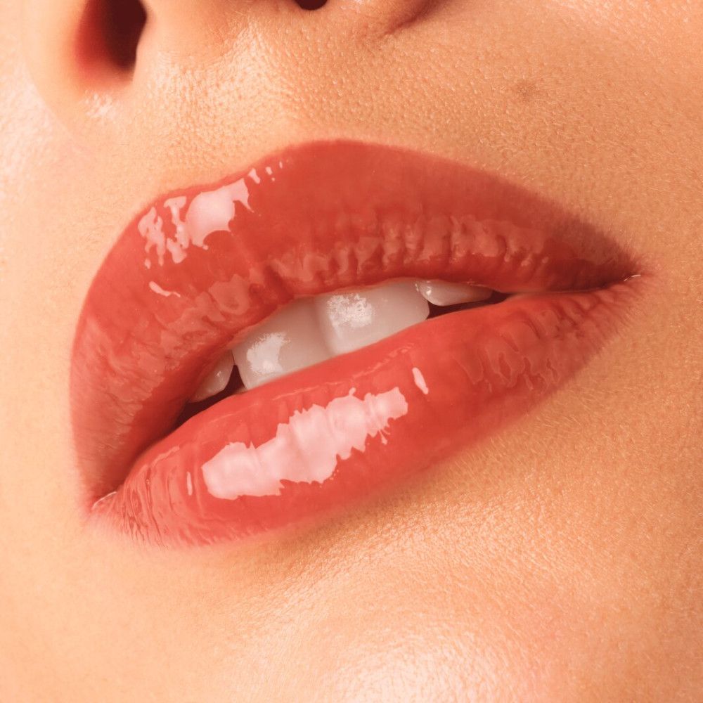 Nahaufnahme von Lippen mit Catrice Supreme Lippenfiller Gloss. Glänzender, orange-brauner Farbton. Geöffnete Lippen, sichtbare Zähne.