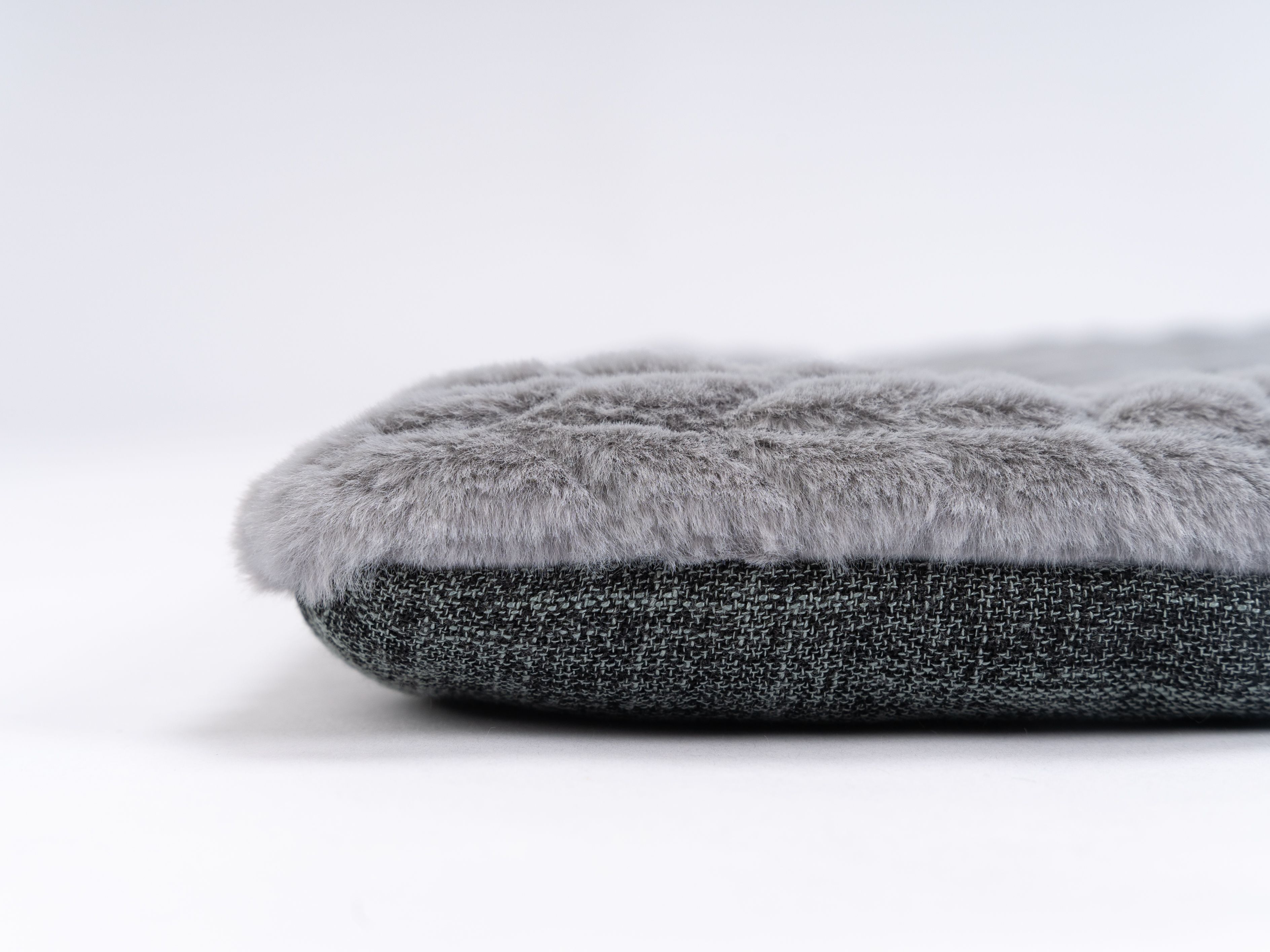 Nahaufnahme einer grauen Liegedecke. Die Oberseite ist flauschig, die Unterseite dunkelgrau.