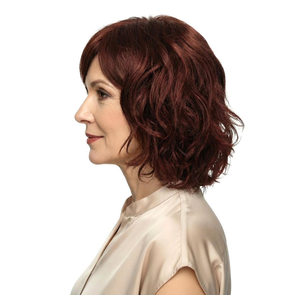 Rote Perücke mit gewelltem Haar. Seitenansicht einer Frau mit hellem Oberteil.