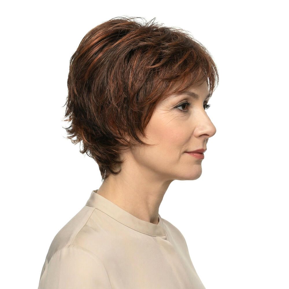 Seitenansicht einer Frau mit kurzer, brauner Perücke mit roten Highlights. Die Frau trägt eine beige Bluse.