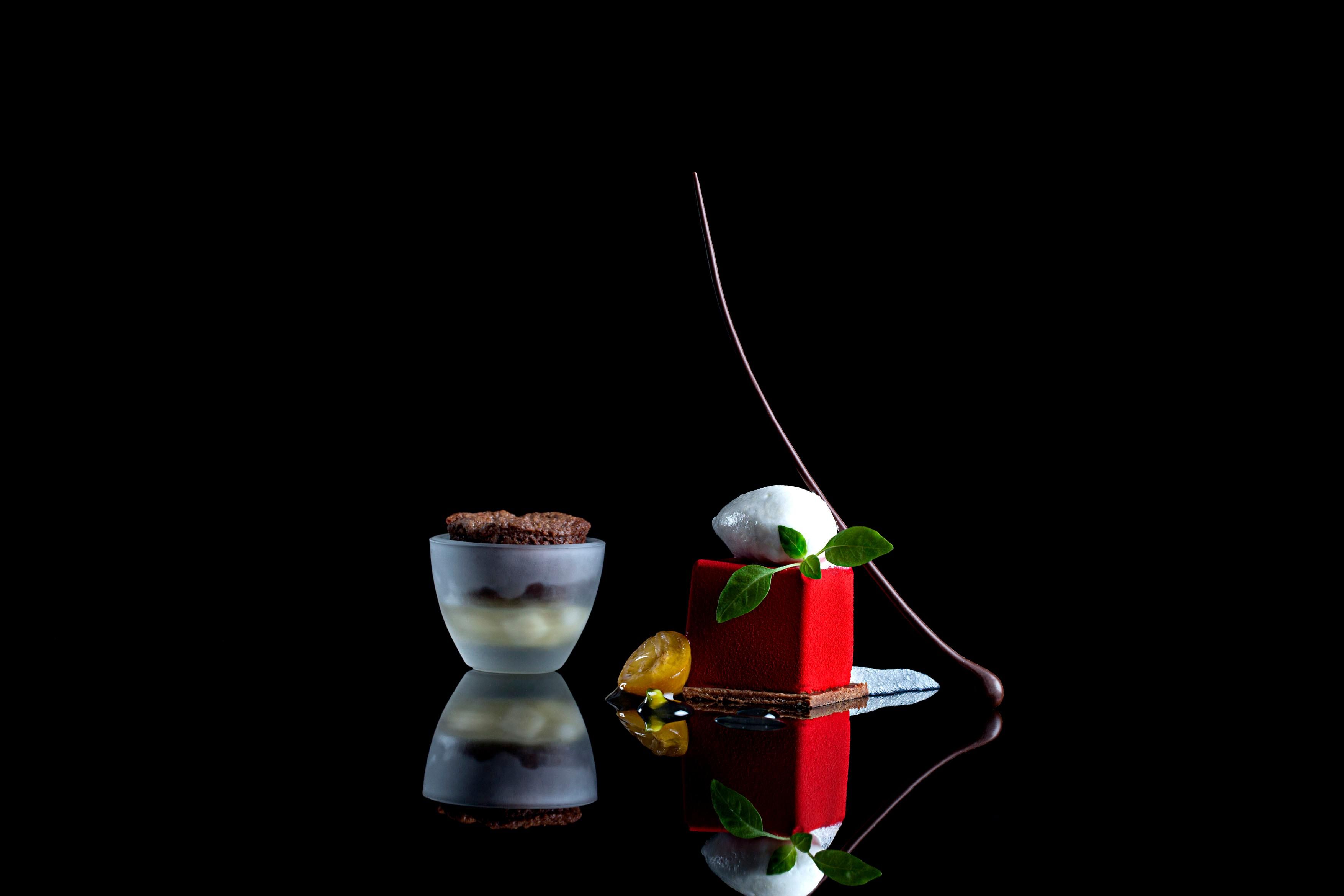 Dessert in Glas und rotem Würfel mit weißer Kugel und Zweig auf schwarzem Untergrund.