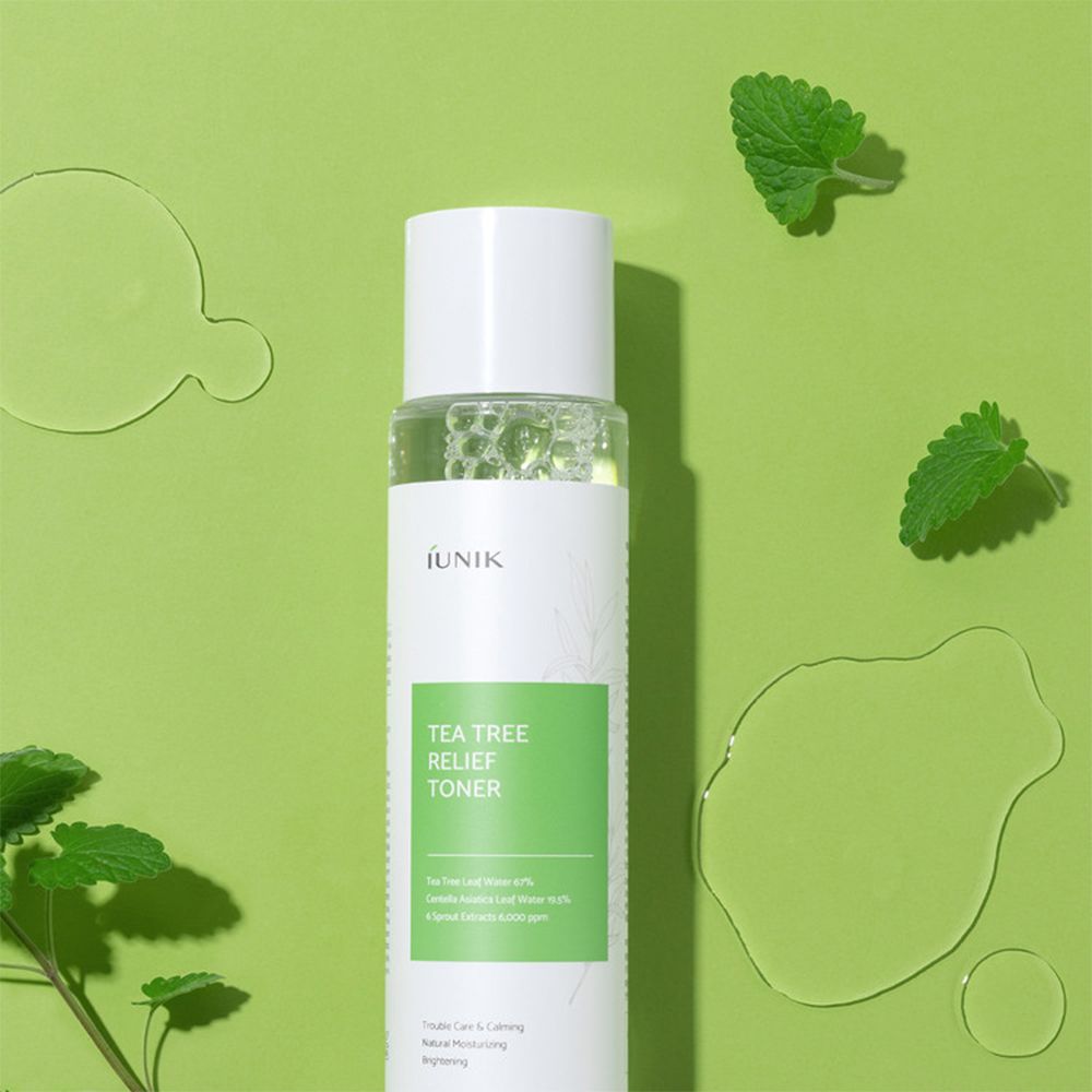 iUNIK Tea Tree Relief Toner auf grünem Hintergrund mit Wassertropfen und Blättern. Klare Flüssigkeit in durchsichtiger Flasche.