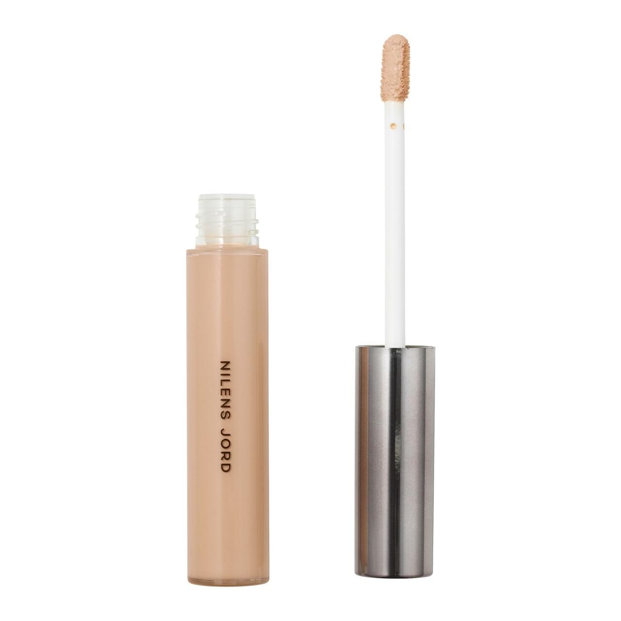 Concealer-Flakon mit Applikator. Beige Flüssigkeit, silberner Deckel. Aufschrift: NILENS JORD.