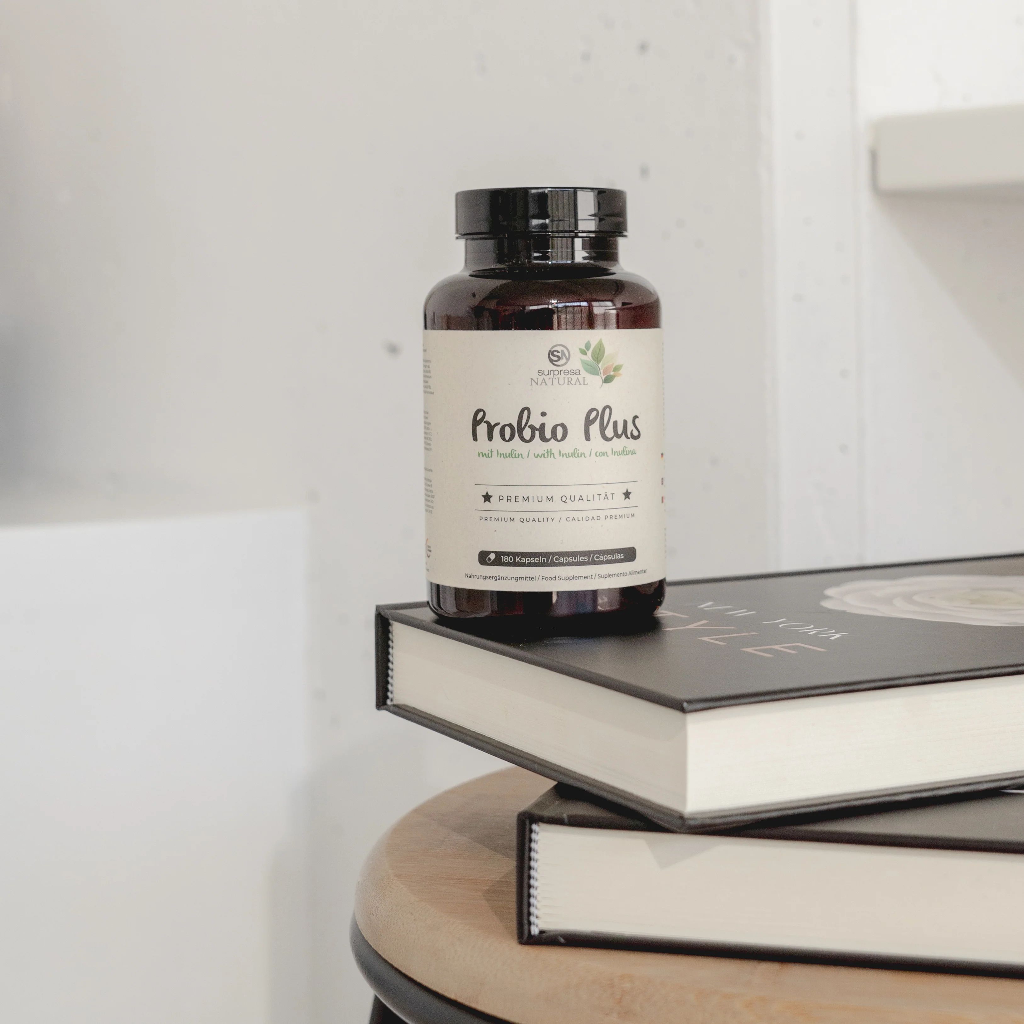 Braune Flasche mit schwarzen Deckel. Aufschrift: Surpresa Natural Probio Plus. Liegt auf Büchern.