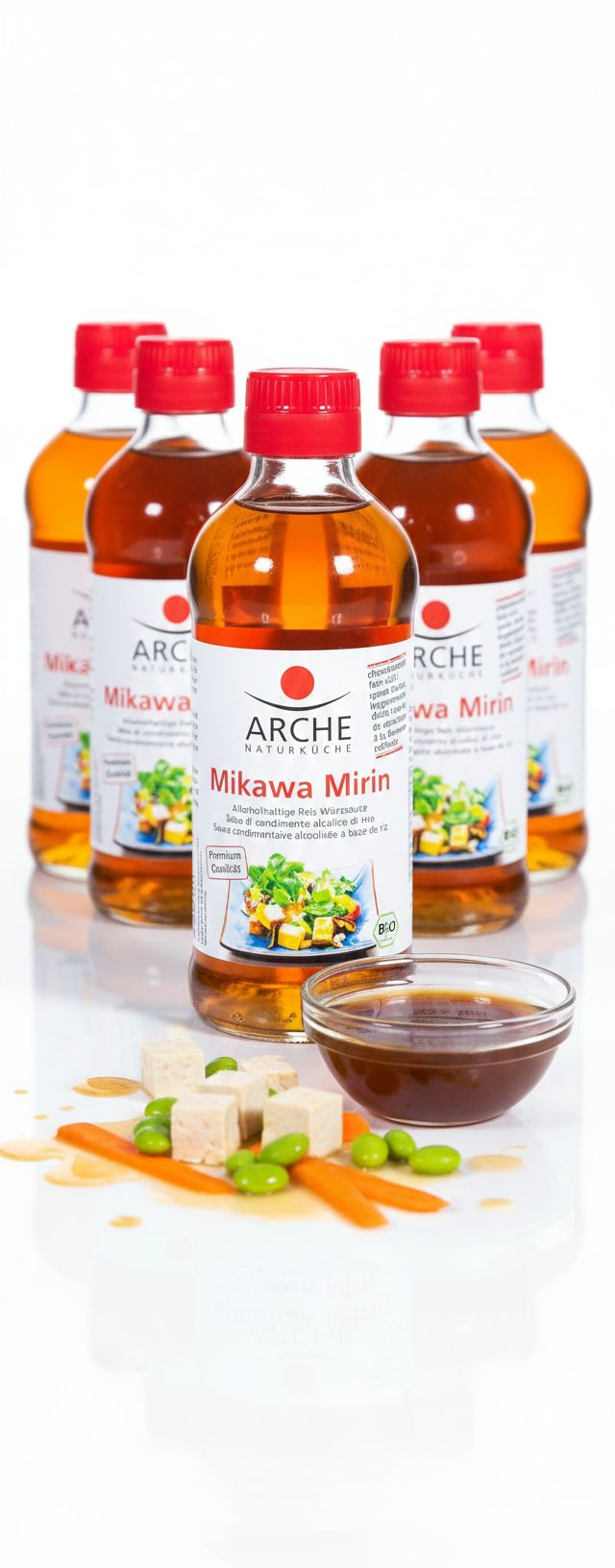 Mehrere Flaschen Arche Mikawa Mirin Reis-Würzsauce, daneben Tofuwürfel, Edamame und Karottenstücke.