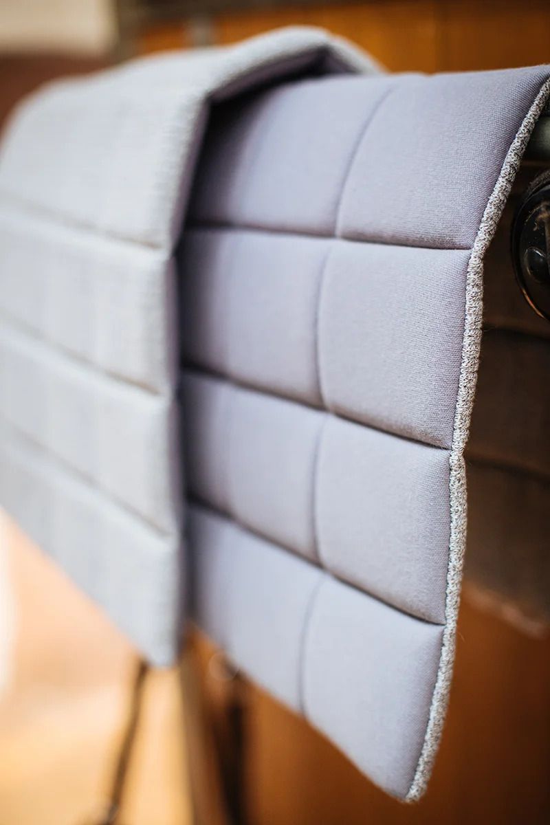 Graues, gepolstertes Pad mit quadratischen Nähten. Der Rand ist mit einem helleren Stoff eingefasst.