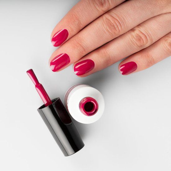 Hand mit lackierten Nägeln in Festive Fuchsia. Nagellackflasche und Pinsel daneben. Pinsel in der Flasche.