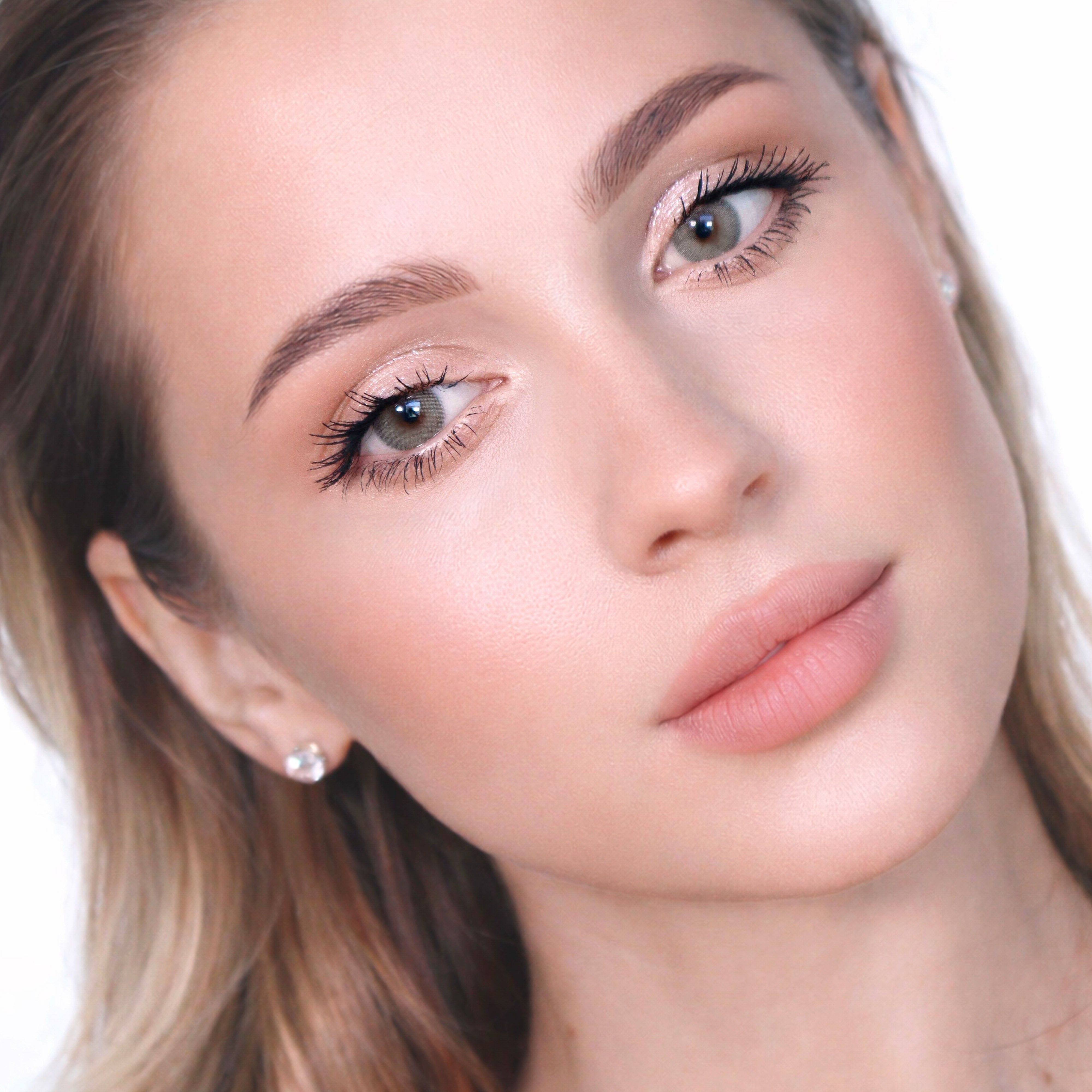 Nahaufnahme einer Frau mit grünlich-grauen Augen. Sie blickt in die Kamera. Ihre Haut ist hell geschminkt.