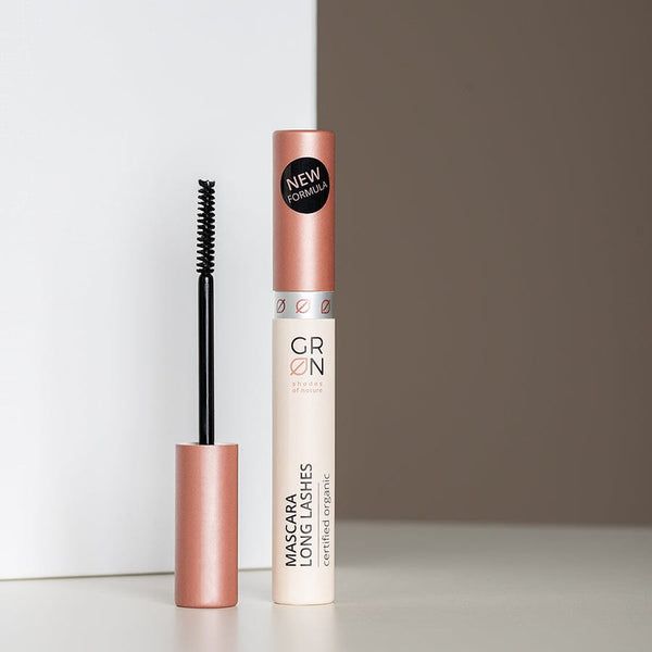 Mascara-Tube mit Bürste. Aufschrift: GRN, Mascara Long Lashes, zertifiziert organisch. Schwarze Bürste, rosafarbener Deckel. Aufschrift: NEW FORMULA.