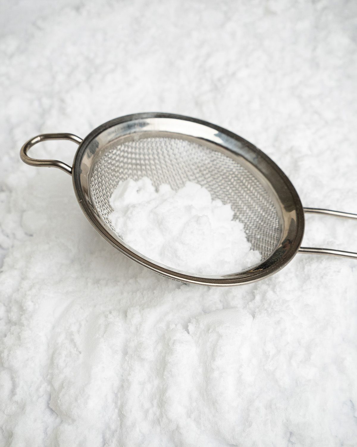 Ein Sieb mit Xylitol Puderzucker auf einem Haufen Puderzucker.