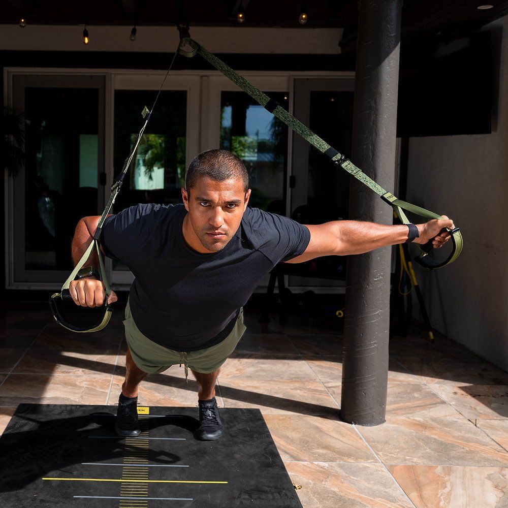 Mann in Sportkleidung macht Liegestütze mit TRX-Schlingentrainer im Freien.