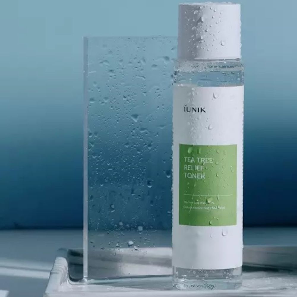 Flacone trasparente con tappo bianco, con gocce d'acqua. Etichetta verde e bianca con testo: IUNIK, Tea Tree Relief Toner.