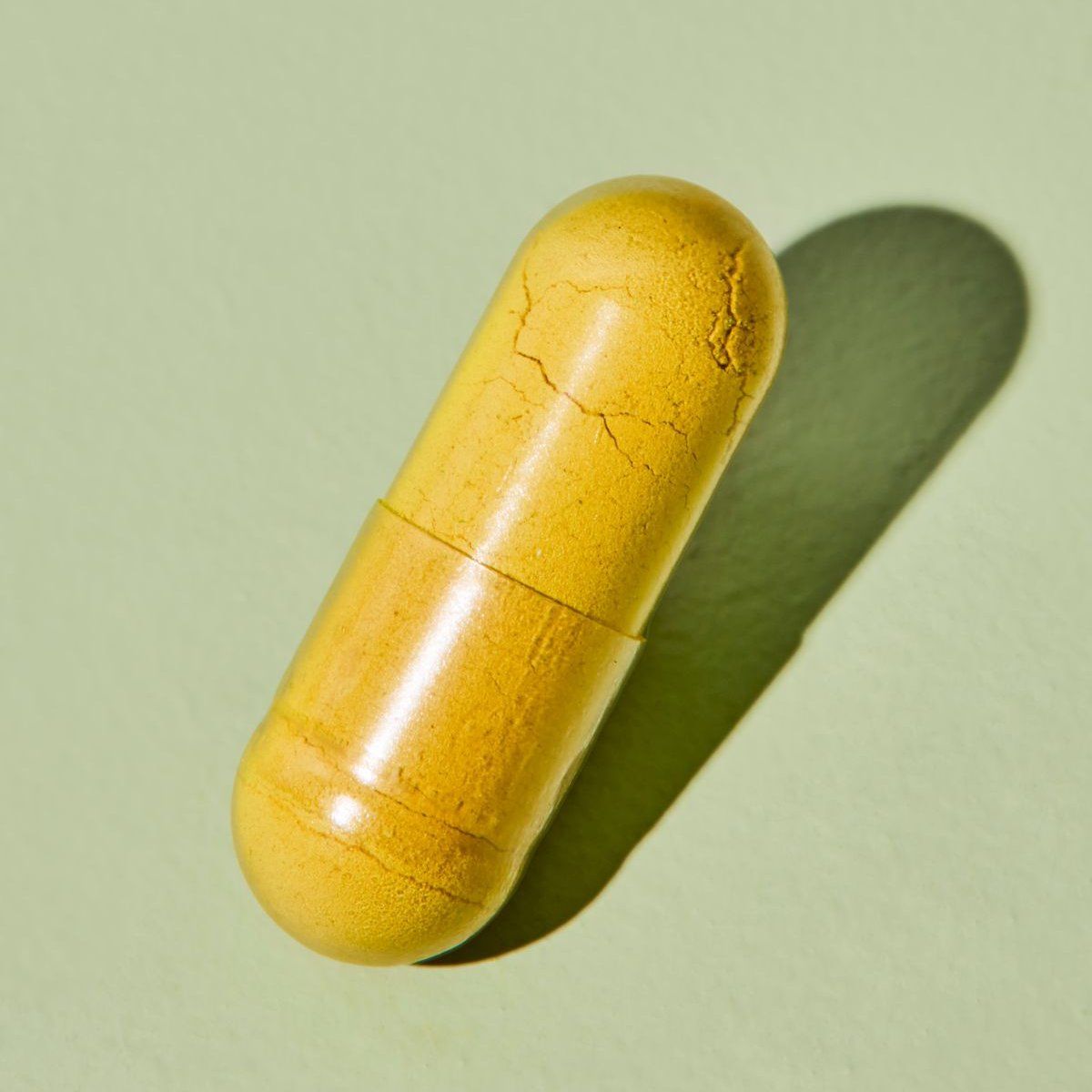 Nahaufnahme einer einzelnen gelben AllergiCare® Daily Kapsel. Kapsel ist zweigeteilt. Schatten auf grünem Hintergrund.