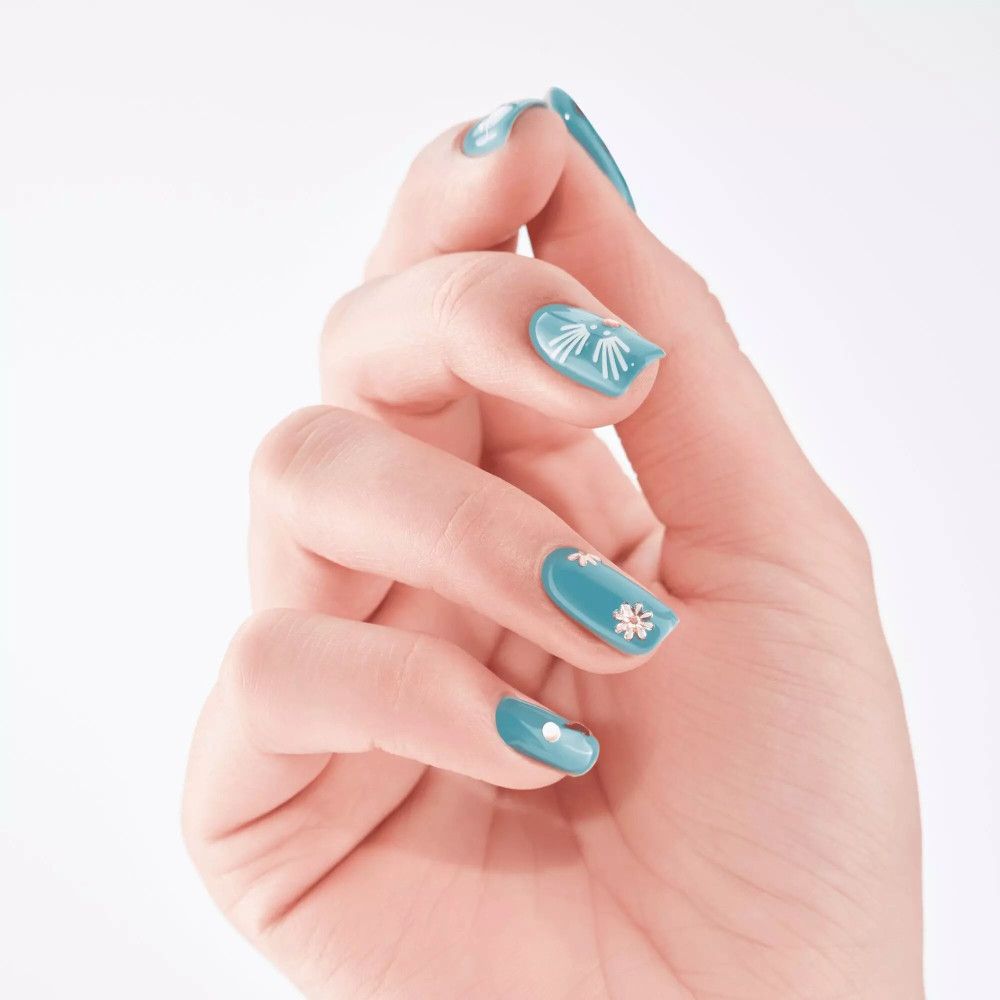 Hand mit türkisfarben lackierten Nägeln. Weiße Nagelsticker in Blüten- und Sternform.