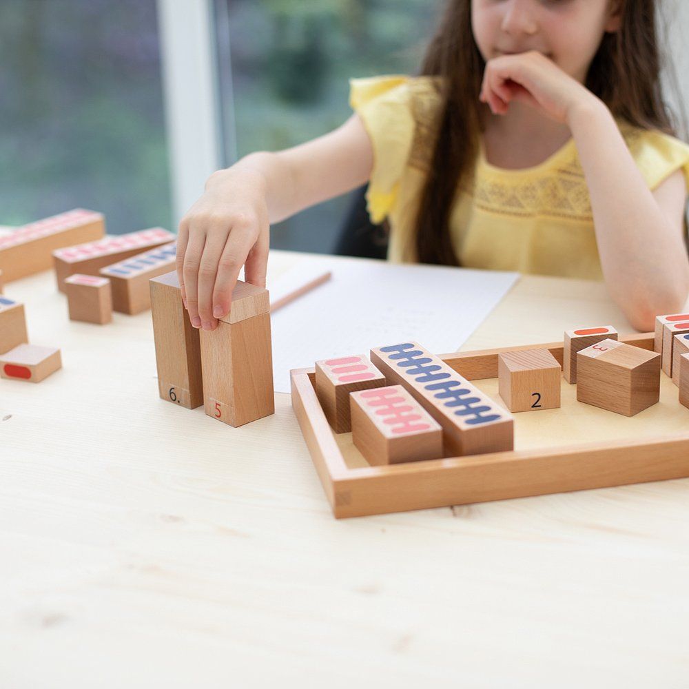 Kind spielt mit Holzbausteinen. Bausteine mit Zahlen und farbigen Markierungen auf einem Tisch. Ein Kind greift nach einem Baustein.